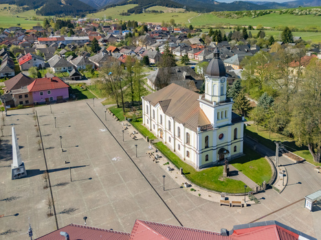 Aerial view of the historic church and main square surrounded by traditional houses and rolling green hills in Partizanska Lupca Zilina Region Slovakia.