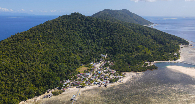 Aerial view of a coastal village nestled between lush green hills and the turquoise waters of Raja Ampat Southwest Papua Indonesia.