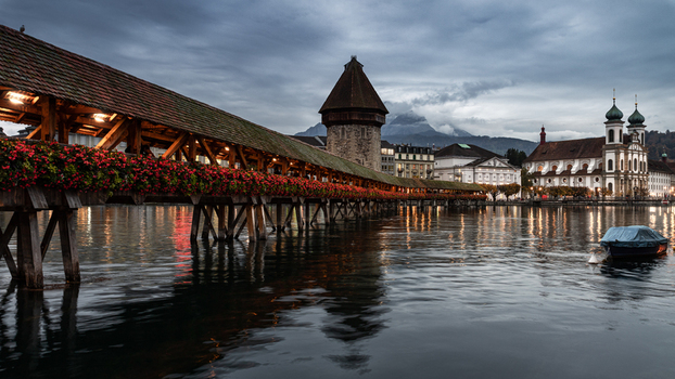 View of the historic Chapel Bridge with red flowers and the Water Tower on the Reuss river with the Jesuit Church in Lucerne Lucerne Switzerland. View of the historic Chapel Bridge with red flowers and the Water Tower on the Reuss river with the Jesuit Church in Lucerne Lucerne Switzerland.