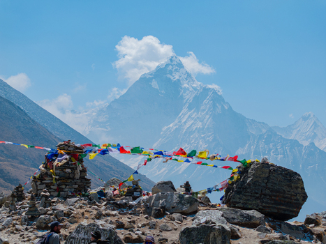 Aerial view of the majestic Ama Dablam mountain peak in the Himalayas featuring colorful prayer flags fluttering in the wind over a rugged rocky landscape in Nepal.