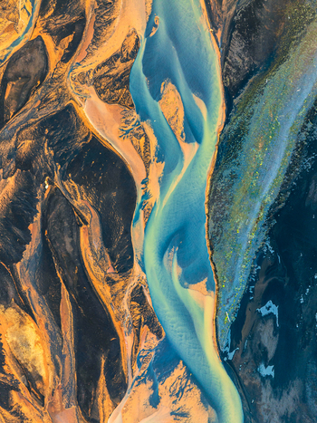 Aerial view of a glacial river featuring intricate patterns of vibrant blue water flowing through dark volcanic sand and orange toned sediment in Iceland. Aerial view of a glacial river featuring intricate patterns of vibrant blue water flowing through dark volcanic sand and orange toned sediment in Iceland.