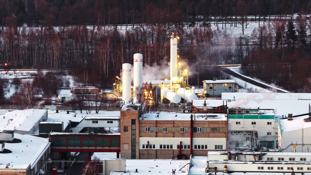 Aerial view of an industrial facility with white gas storage tanks and steam rising from the plant set against a snowy forest landscape in Latvia. Aerial view of an industrial facility with white gas storage tanks and steam rising from the plant set against a snowy forest landscape in Latvia.