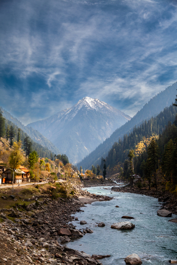 View of the Neelum River flowing through the Neelum Valley towards a snow capped mountain peak under a blue sky with wispy clouds Arang Kel Azad Kashmir Pakistan. View of the Neelum River flowing through the Neelum Valley towards a snow capped mountain peak under a blue sky with wispy clouds Arang Kel Azad Kashmir Pakistan.