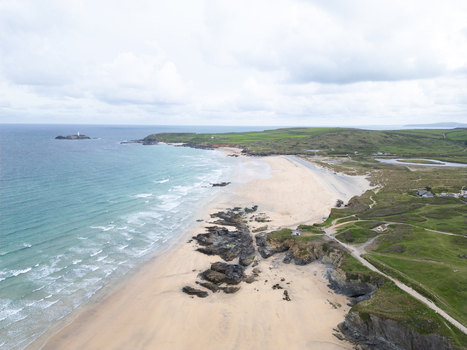 Aerial view of Godrevy Beach featuring sandy shores dark rocky outcrops and turquoise waves under an overcast sky with Godrevy Lighthouse in the distance Gwithian England United Kingdom. Aerial view of Godrevy Beach featuring sandy shores dark rocky outcrops and turquoise waves under an overcast sky with Godrevy Lighthouse in the distance Gwithian England United Kingdom.