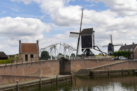 View of a traditional Dutch windmill and a white drawbridge over a canal with historic brick fortifications in Heusden North Brabant Netherlands.