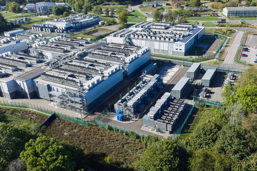 Aerial view of a large data center facility with industrial cooling units server buildings and security fencing in the United Kingdom.