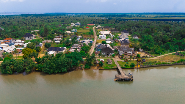 Aerial view of a coastal village with houses lush trees and a small concrete pier extending into the river in Minima Rivers Nigeria.