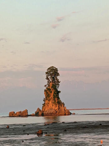 View of the iconic Onna iwa rock formation at Amaharashi Coast illuminated by warm sunset light with calm waters in Takaoka Toyama Japan.