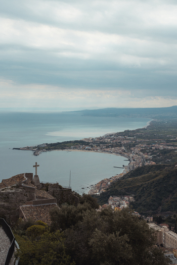 View of a rugged coastline embracing the serene sea stone structures standing guard under a cloudy sky in Taormina Catania Italy. View of a rugged coastline embracing the serene sea stone structures standing guard under a cloudy sky in Taormina Catania Italy.