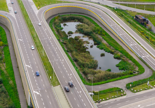 Aerial view of a highway interchange with a U turn loop and a small pond in the center surrounded by green grass and concrete walls in Gdansk Pomeranian Voivodeship Poland. Aerial view of a highway interchange with a U turn loop and a small pond in the center surrounded by green grass and concrete walls in Gdansk Pomeranian Voivodeship Poland.