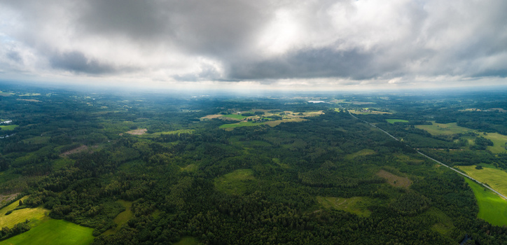 Aerial view of the vast green forests agricultural fields and a winding road under a dramatic cloudy sky in Latvia. Aerial view of the vast green forests agricultural fields and a winding road under a dramatic cloudy sky in Latvia.