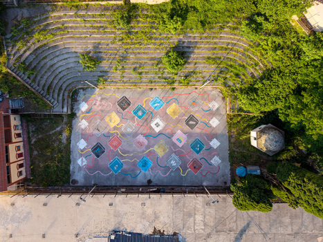 Aerial view of a colorful outdoor sports court with geometric murals and stone amphitheater seating surrounded by lush green trees in Kruje Durres County Albania.