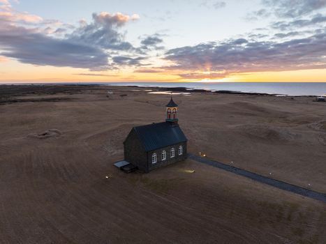 Aerial view of Hvalsneskirkja church standing in a vast barren landscape under a golden sunset sky in Sudurnesjabaer Iceland. Aerial view of Hvalsneskirkja church standing in a vast barren landscape under a golden sunset sky in Sudurnesjabaer Iceland.