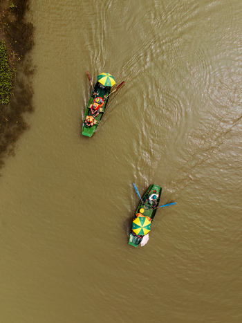 Aerial view of two small boats with people and colorful umbrellas rowing on a river in Vietnam. Aerial view of two small boats with people and colorful umbrellas rowing on a river in Vietnam.