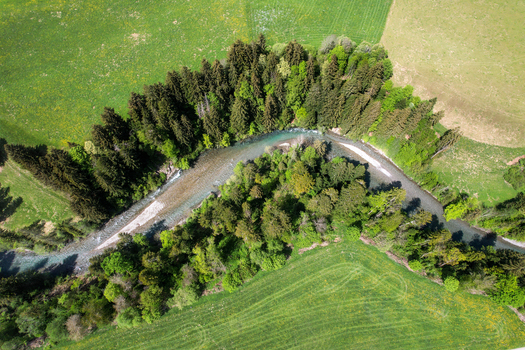 Aerial view of a winding river flowing through a lush green forest and vibrant meadows in Rougemont Vaud Switzerland. Aerial view of a winding river flowing through a lush green forest and vibrant meadows in Rougemont Vaud Switzerland.