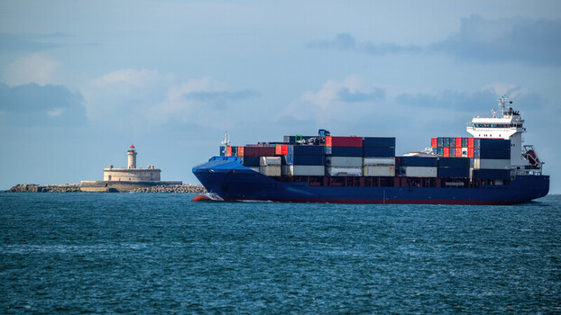 View of a large container ship with colorful cargo containers sailing past the Bugio Lighthouse under a cloudy sky in Lisbon Lisbon Portugal. View of a large container ship with colorful cargo containers sailing past the Bugio Lighthouse under a cloudy sky in Lisbon Lisbon Portugal.