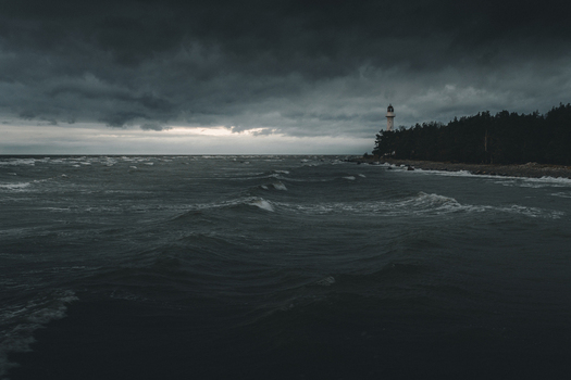 View of Saxby Lighthouse standing on the rocky coastline under a dark stormy sky with turbulent waves crashing on the shore in Saxby Laane maakond Estonia.