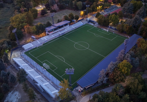 Aerial view of Mladost Sports Center featuring a green soccer pitch stadium seating and surrounding trees in Pancevo Serbia. Aerial view of Mladost Sports Center featuring a green soccer pitch stadium seating and surrounding trees in Pancevo Serbia.