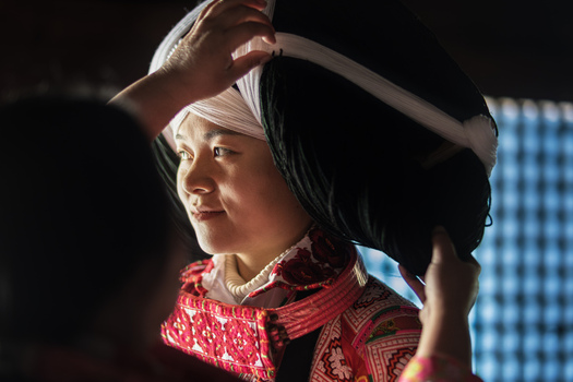 Gaoxing China 30 April 2026 View of a Long Horn Miao woman in traditional embroidered dress having her large black and white headpiece adjusted by another person. Gaoxing China 30 April 2026 View of a Long Horn Miao woman in traditional embroidered dress having her large black and white headpiece adjusted by another person.