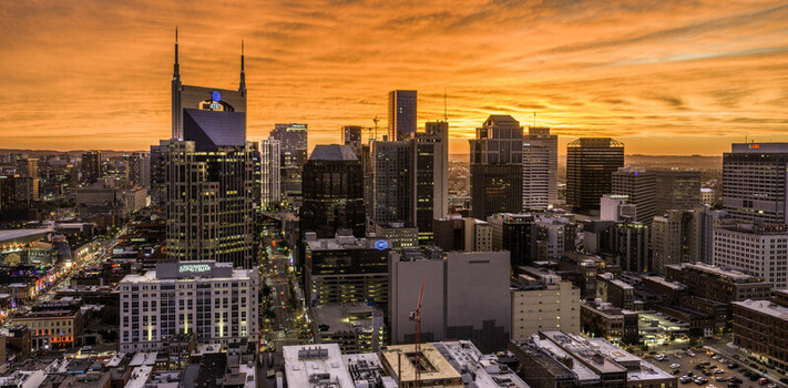 Aerial view of the downtown Nashville skyline at sunset featuring the iconic ATT Building modern skyscrapers urban streets and a vibrant orange sky in Nashville TN United States.