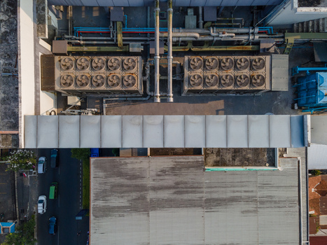 Aerial view of industrial building rooftop featuring large HVAC cooling fan units ventilation pipes and a street with vehicles below in Purwokerto Central Java Indonesia. Aerial view of industrial building rooftop featuring large HVAC cooling fan units ventilation pipes and a street with vehicles below in Purwokerto Central Java Indonesia.