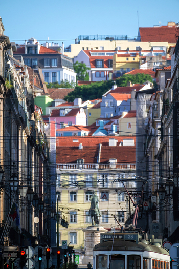 View of a traditional yellow tram on a narrow street leading to the Praca do Comercio with colorful houses on the hill in Lisbon Lisbon Portugal.