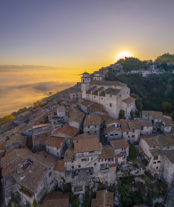 Aerial view of the historic town of Artena with stone buildings and terracotta rooftops at sunrise set against rolling hills and morning mist in Artena Lazio Italy.
