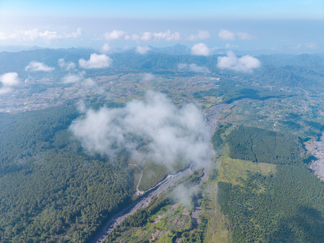 Aerial view of the Sumberurip area featuring dense green forests a winding river valley and scattered clouds over the mountainous landscape of Pronojiwo East Java Indonesia. Aerial view of the Sumberurip area featuring dense green forests a winding river valley and scattered clouds over the mountainous landscape of Pronojiwo East Java Indonesia.