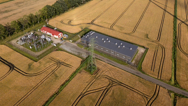 Aerial view of industrial battery energy storage system BESS facility integrated with wind farm power grid infrastructure in rural landscape. Aerial view of industrial battery energy storage system BESS facility integrated with wind farm power grid infrastructure in rural landscape.