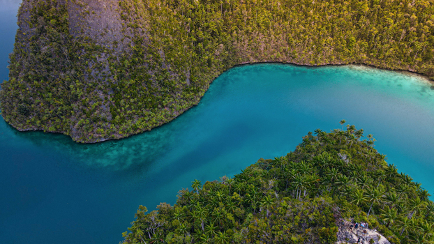 Aerial view of a tropical lagoon with turquoise water surrounded by lush green karst islands and dense vegetation in Indonesia. Aerial view of a tropical lagoon with turquoise water surrounded by lush green karst islands and dense vegetation in Indonesia.