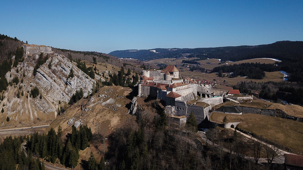Aerial view of the historic Chateau de Joux fortress perched on a rocky hill surrounded by rolling hills and forests in La Cluse et Mijoux Bourgogne Franche Comte France. Aerial view of the historic Chateau de Joux fortress perched on a rocky hill surrounded by rolling hills and forests in La Cluse et Mijoux Bourgogne Franche Comte France.