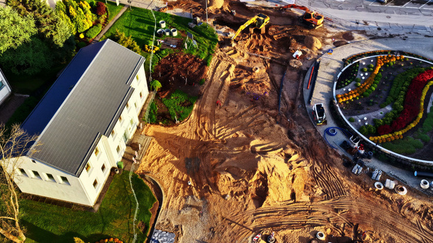 Aerial view of a construction site with an excavator piles of earth and a building next to a circular flower bed in Latvija. Aerial view of a construction site with an excavator piles of earth and a building next to a circular flower bed in Latvija.