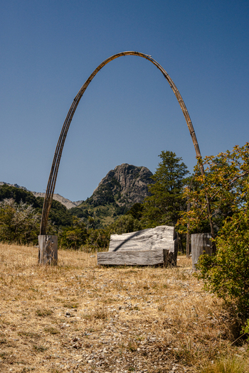 View of a rustic wooden arch and carved log bench in a dry grassy field with a rocky mountain peak near Lago Paimun Huiliches Department Neuquen Province Argentina.