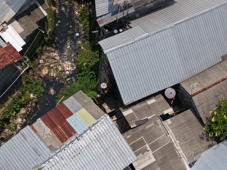 Aerial view of a narrow canal flowing between residential houses with corrugated metal roofs in Kecamatan Denpasar Barat Bali Indonesia. Aerial view of a narrow canal flowing between residential houses with corrugated metal roofs in Kecamatan Denpasar Barat Bali Indonesia.
