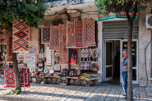 Kruje Albania 12 June 2026 View of a traditional souvenir shop displaying colorful handmade rugs and bags in the historic Old Bazaar with a man standing by the entrance.