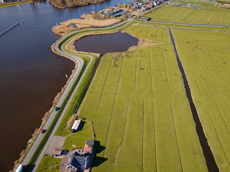 Aerial view of lush green fields meet dark waters divided by a winding road under a clear sky Nature reserve Schaalsmeerpolder Wormer Netherlands. Aerial view of lush green fields meet dark waters divided by a winding road under a clear sky Nature reserve Schaalsmeerpolder Wormer Netherlands.