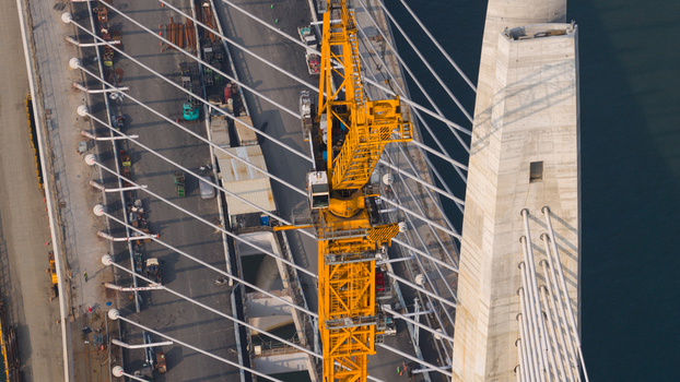 Aerial view of the Danjiang Bridge construction site featuring a prominent yellow crane cable stayed pylon and construction equipment in Tamsui District New Taipei City Taiwan.