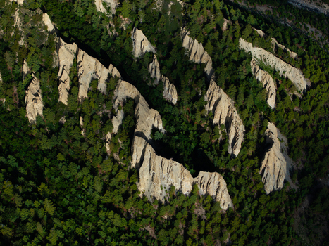 Aerial view of sharp eroded rock formations rising through a dense green forest in Nepal.