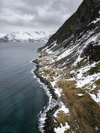 Aerial view of Grotfjord coastline with snow dusted mountains rocky shores and dark blue sea under a cloudy sky Tromvik Troms Norway. Aerial view of Grotfjord coastline with snow dusted mountains rocky shores and dark blue sea under a cloudy sky Tromvik Troms Norway.
