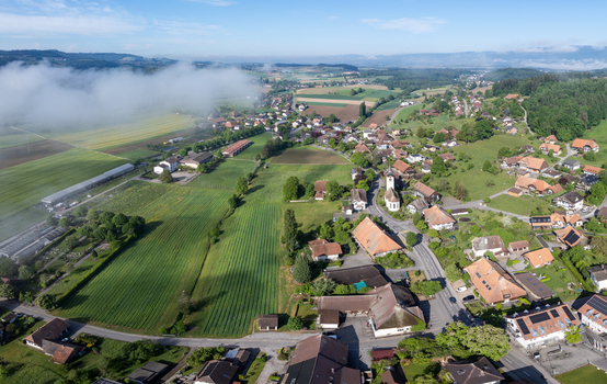 Aerial view of the village of Grossaffoltern featuring traditional houses a church steeple and lush green agricultural fields under a misty morning sky Grossaffoltern Canton of Bern Switzerland. Aerial view of the village of Grossaffoltern featuring traditional houses a church steeple and lush green agricultural fields under a misty morning sky Grossaffoltern Canton of Bern Switzerland.