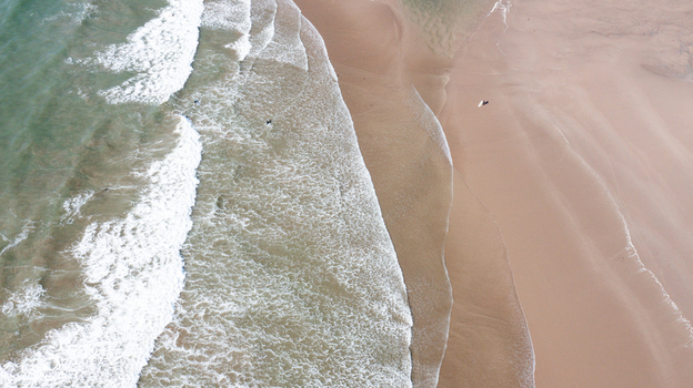 Aerial view of Bantham Beach with waves crashing on the sandy shore and surfers in the water in Kingsbridge Devon United Kingdom. Aerial view of Bantham Beach with waves crashing on the sandy shore and surfers in the water in Kingsbridge Devon United Kingdom.