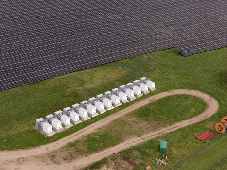 Aerial view of a battery energy storage system with white units arranged in a row next to a large solar farm in Poland. Aerial view of a battery energy storage system with white units arranged in a row next to a large solar farm in Poland.
