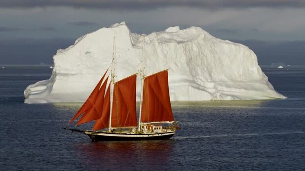 Aerial view of sailboat with red sails near iceberg in Greenland. Aerial view of sailboat with red sails near iceberg in Greenland.