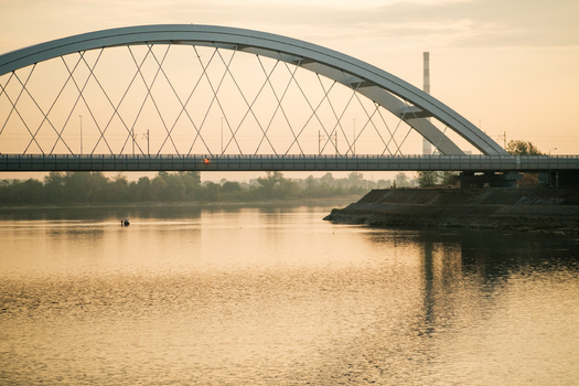 View of the Zezelj Bridge spanning the Danube River at sunset with a calm water surface and industrial chimney in the background in Novi Sad Vojvodina Serbia. View of the Zezelj Bridge spanning the Danube River at sunset with a calm water surface and industrial chimney in the background in Novi Sad Vojvodina Serbia.