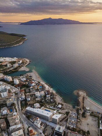 Aerial view of the coastal city with its hotels buildings and beach along the Ionian Sea during a golden sunset in Saranda Vlore County Albania. Aerial view of the coastal city with its hotels buildings and beach along the Ionian Sea during a golden sunset in Saranda Vlore County Albania.