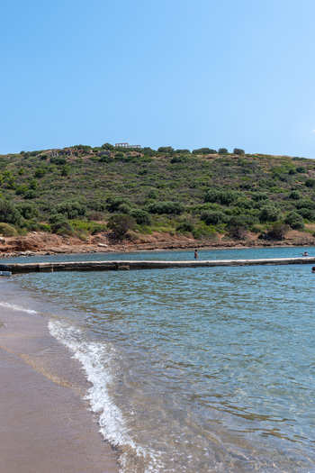 View of the Temple of Poseidon at Cape Sounio on a green hill overlooking a sandy beach and clear blue sea water in Sounion Greece.