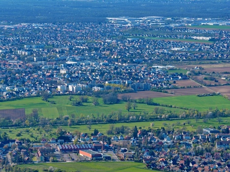 Aerial view of a patchwork of fields meet urban sprawl a symphony of greens and greys under the vast sky Sausheim Grand Est France.