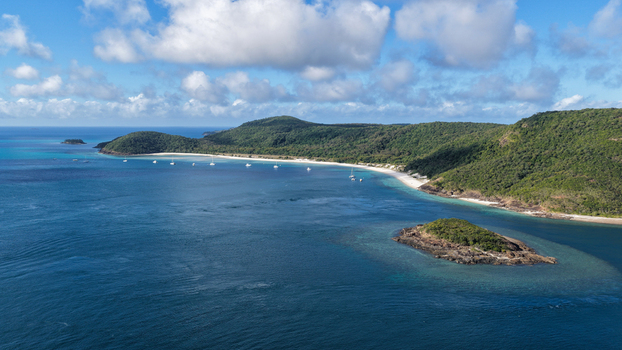Aerial view of Haslewood Island with lush green hills white sandy beaches and turquoise waters with boats anchored in the bay under a blue sky Whitsundays Queensland Australia. Aerial view of Haslewood Island with lush green hills white sandy beaches and turquoise waters with boats anchored in the bay under a blue sky Whitsundays Queensland Australia.