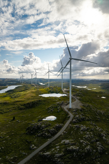 Aerial view of Makaknuten Vindkraftverk wind farm with large wind turbines standing on a rocky green landscape with small ponds and a winding road in Bjerkreim Municipality Rogaland Norway. Aerial view of Makaknuten Vindkraftverk wind farm with large wind turbines standing on a rocky green landscape with small ponds and a winding road in Bjerkreim Municipality Rogaland Norway.