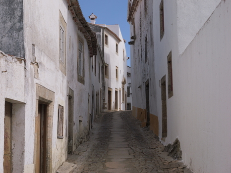 View of the narrow cobblestone street lined with historic white washed buildings and stone architectural details in the hilltop town of Marvao Portalegre District Portugal. View of the narrow cobblestone street lined with historic white washed buildings and stone architectural details in the hilltop town of Marvao Portalegre District Portugal.